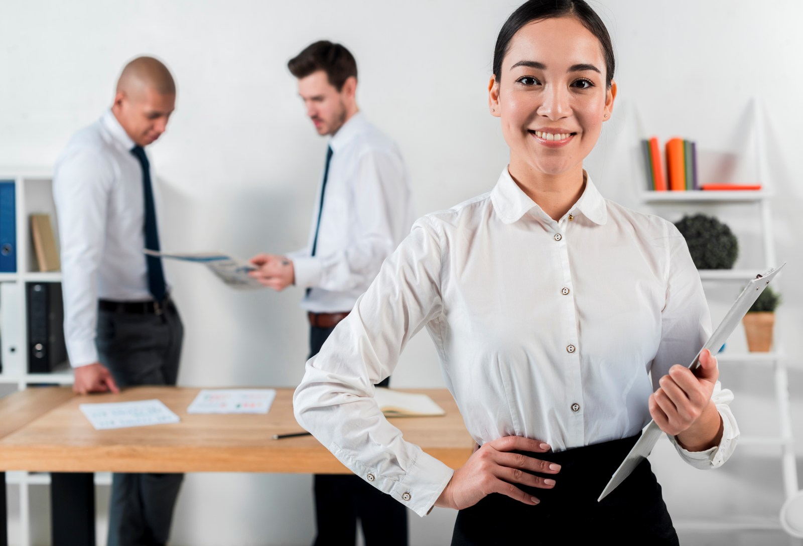 confident-smiling-young-businesswoman-holding-clipboard-hand-with-two-businessman-standing-backdrop